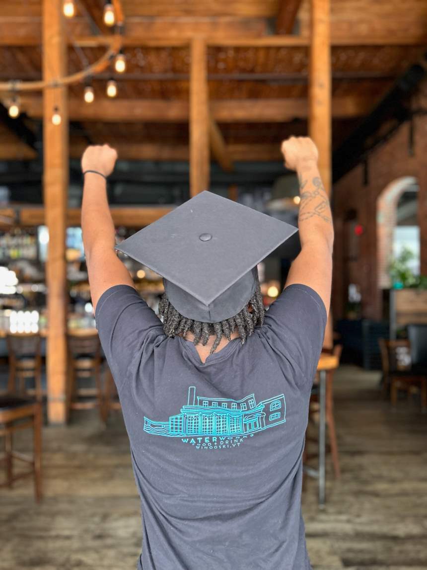A photo of someone from behind with both arms in the air, wearing a graduation cap